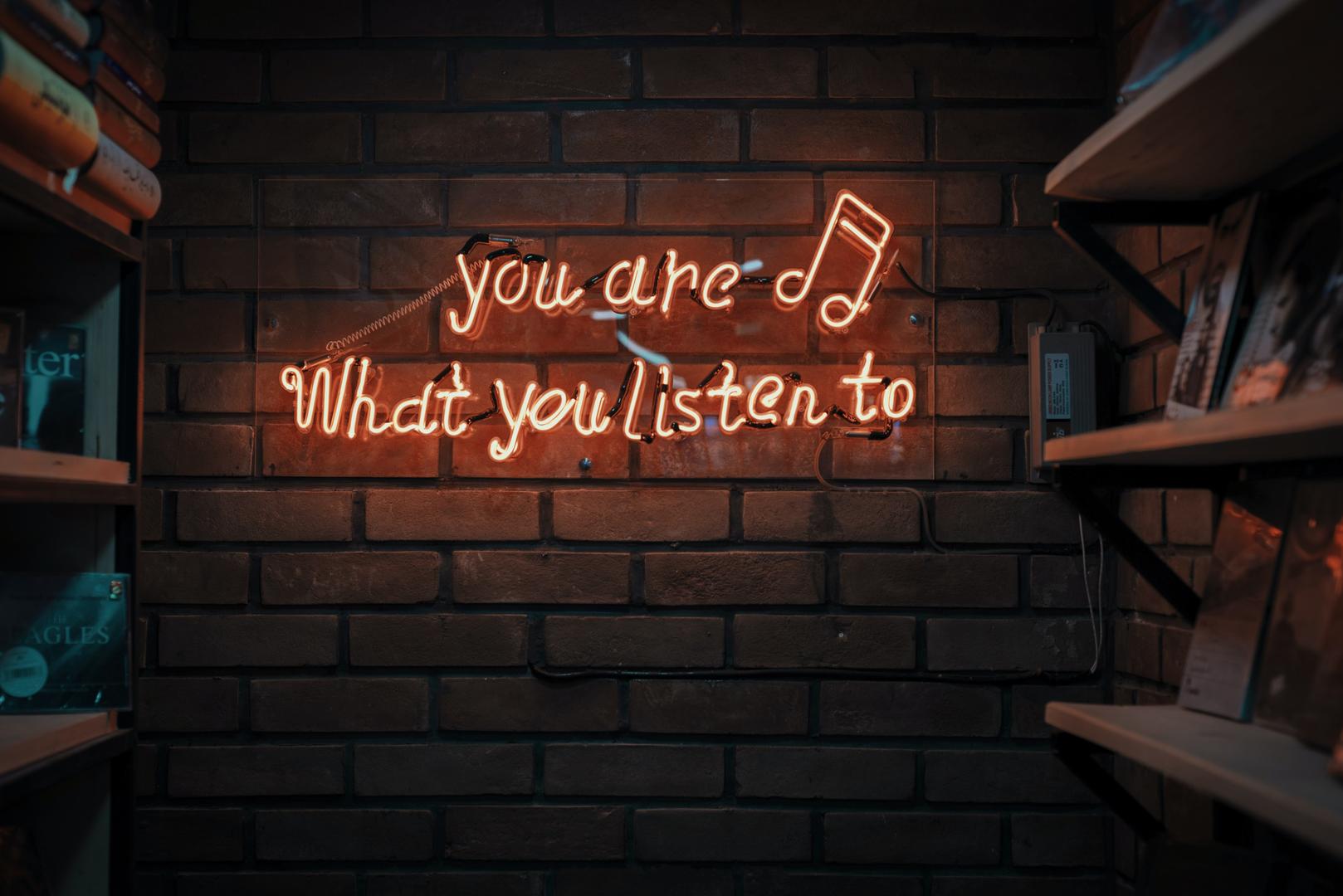 Neonschriftzug "you are what you listen to" an Backsteinwand