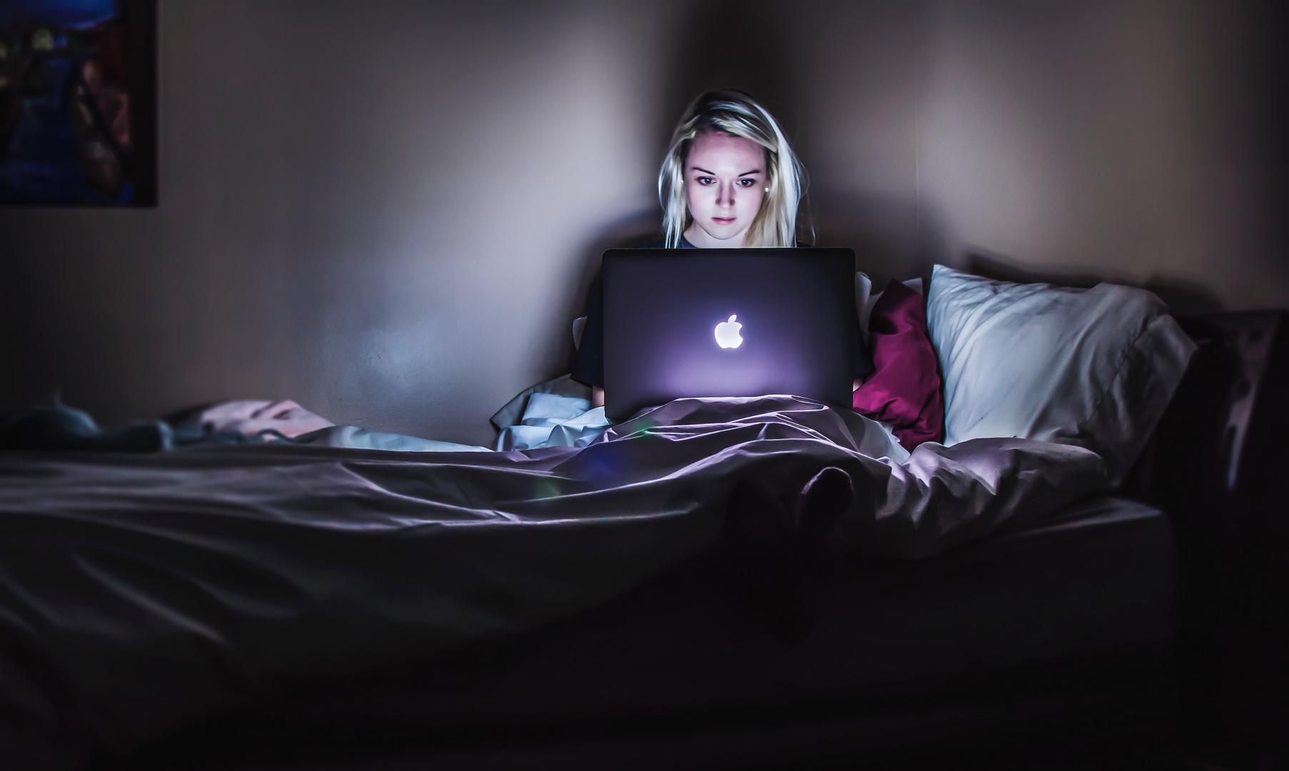 Mädchen im Bett vor dem Laptop im Dunklen