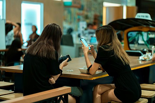 Zwei Mädhen sitzen vor ihren Handys an einem Pausentisch in der Schule