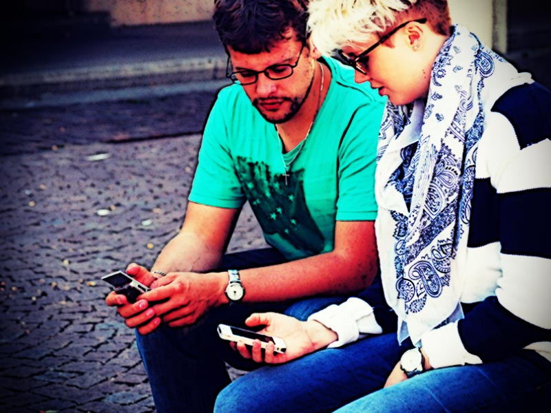 Jugendliche sitzen mit Smartphone im Freien